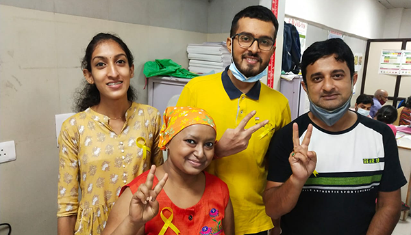 A photo of four people, two women and two men, all members of the Sachin Sarcoma Society, posing for a photo in a hospital in India during the pandemic. All are wearing yellow ribbons to symbolise sarcoma awareness and companionship.