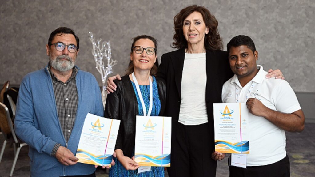 Four people pose for a photo with certificates of recognition that have just been awarded.