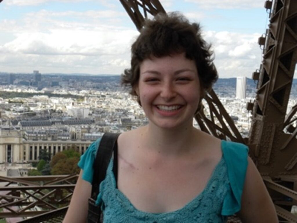 A photo of a smiling Abbie Basson standing on the viewing platform of the Eiffel Tower overlooking Paris.